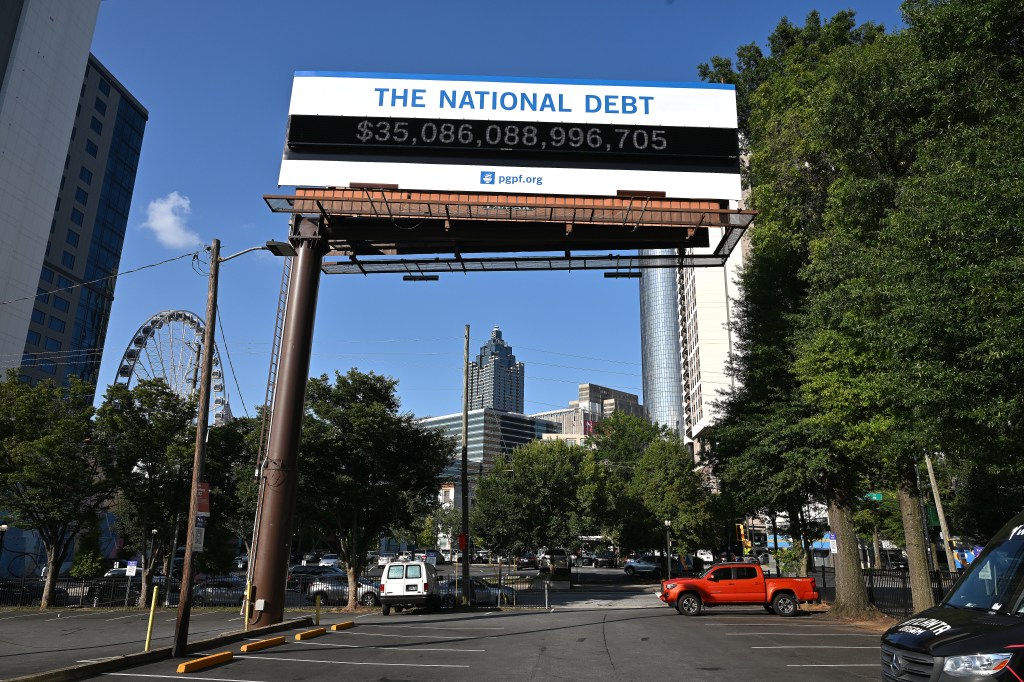 A poster and electronic billboard displayed near Ted Turner Dr and Marietta St that displays the current U.S. National debt per person and as a nation at 35 Trillion dollars on August 08, 2024 in Atlanta, Georgia.