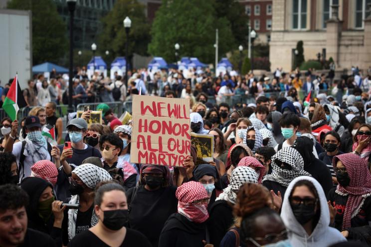 Group of pro-Palestinian demonstrators wearing masks and holding a sign on the campus of Columbia University, marking the one-year anniversary of Hamas' October 7 attack