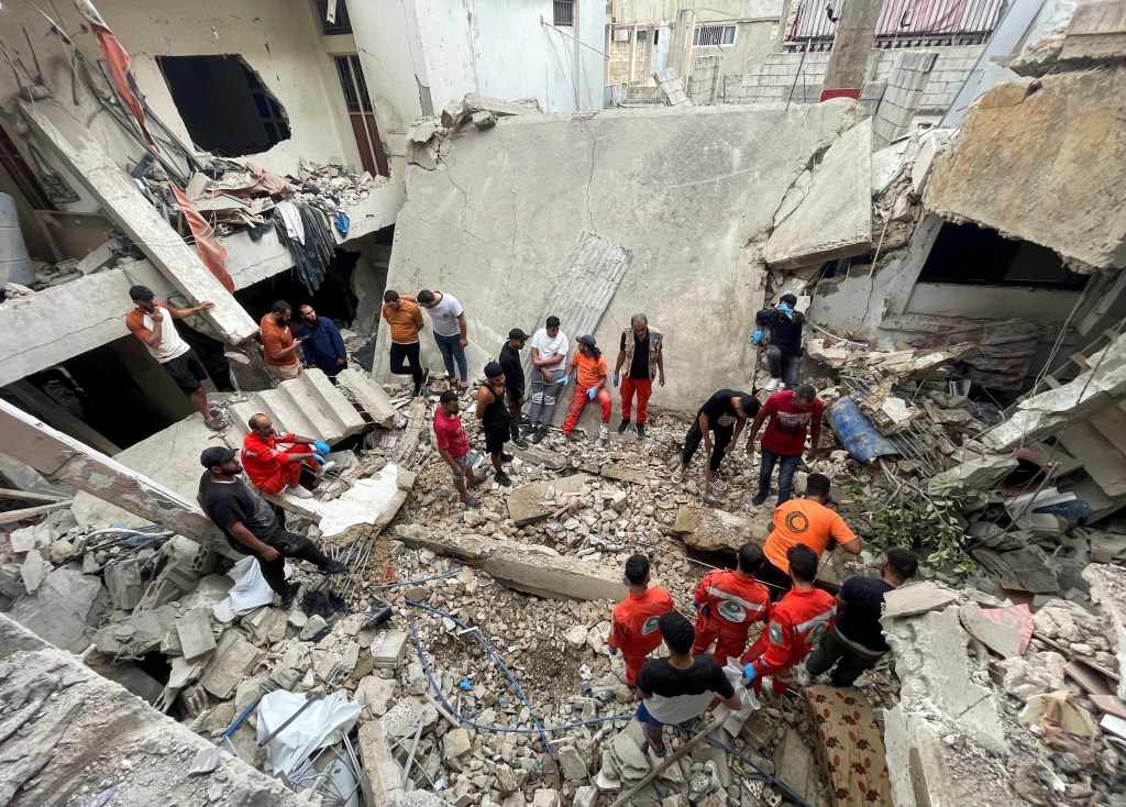 Rescuers and people inspect the site of a strike in Ain al-Hilweh refugee camp, near the southern city of Sidon.