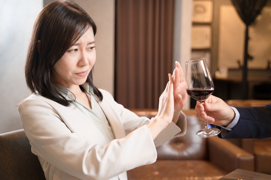 A woman rejects a glass of wine. 