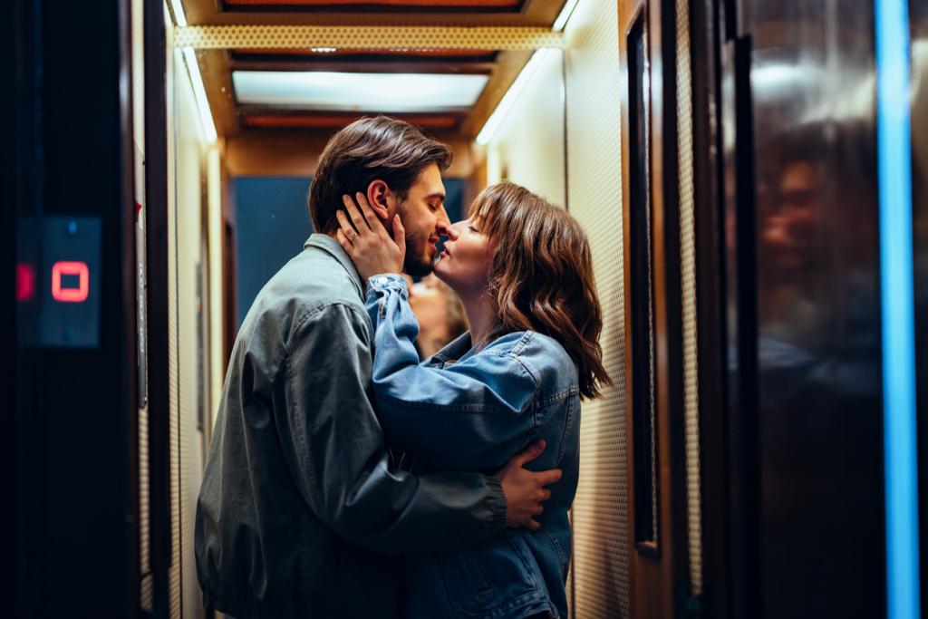 A happy couple laughing and exchanging a kiss while embracing each other in an elevator.