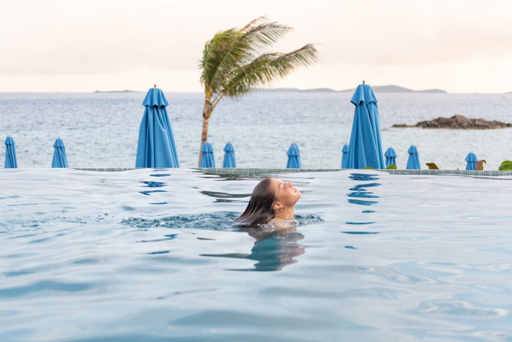 A woman swimming in Lovango Resort's infinity pool with a palm tree in the background.