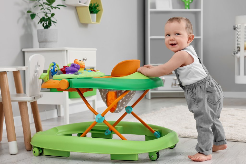 A baby making their first steps with the aid of a toy walker at home