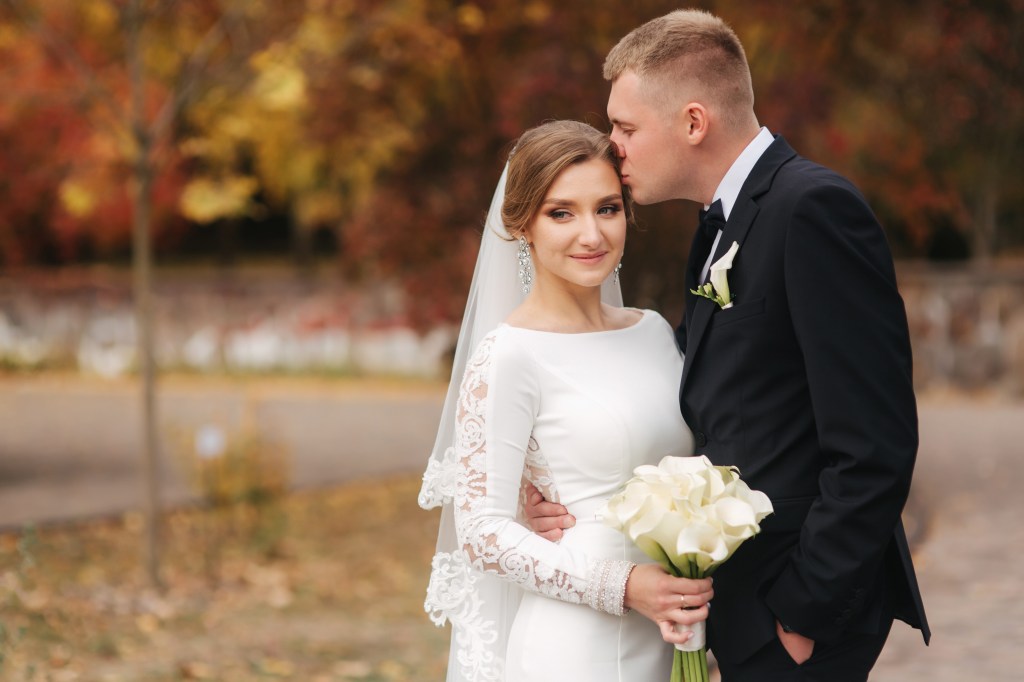 Happy newlyweds walking in a park on their wedding day, surrounded by autumn leaves in yellow and red hues