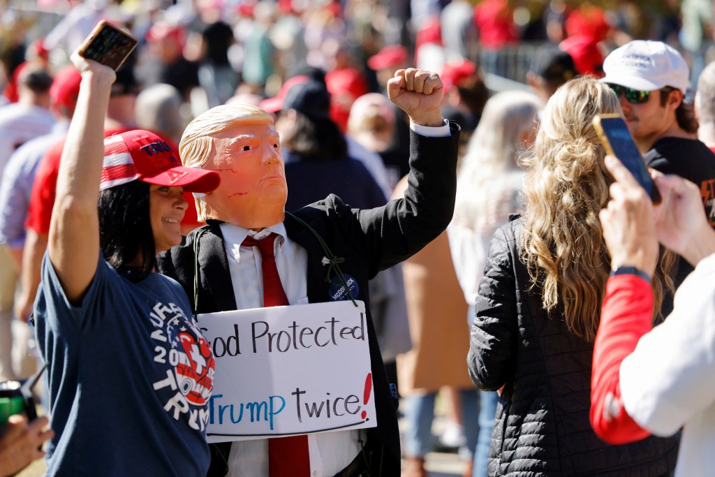 Supporter of Donald Trump wearing a Trump mask and holding a sign referencing two assassination attempts, at a campaign rally in Greenville, North Carolina on October 21, 2024