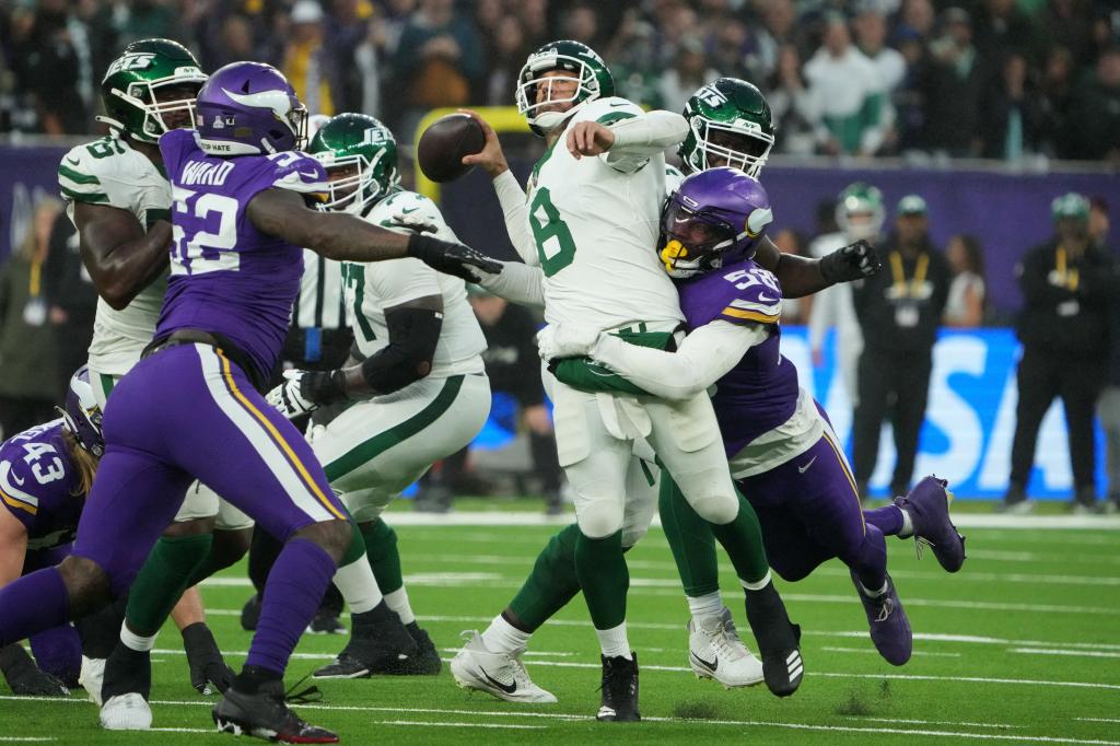 Aaron Rodgers of the New York Jets throwing a football under pressure from Minnesota Vikings linebacker Jonathan Greenard, during a game at Tottenham Hotspur Stadium in London.