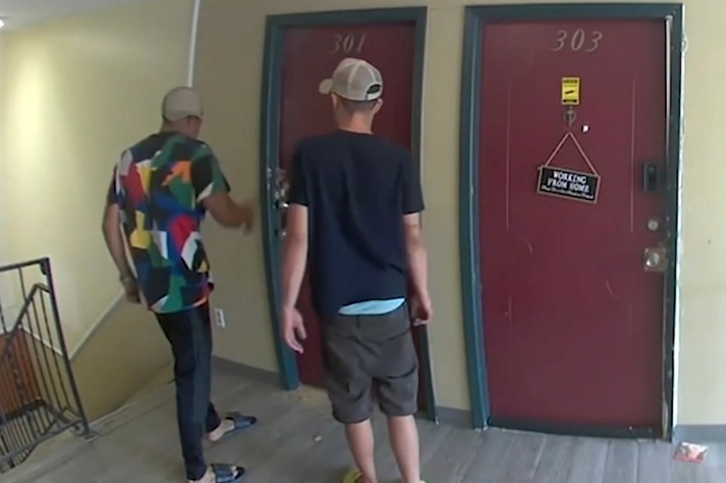 A man standing in front of two doors at an apartment complex, video footage from gang activity