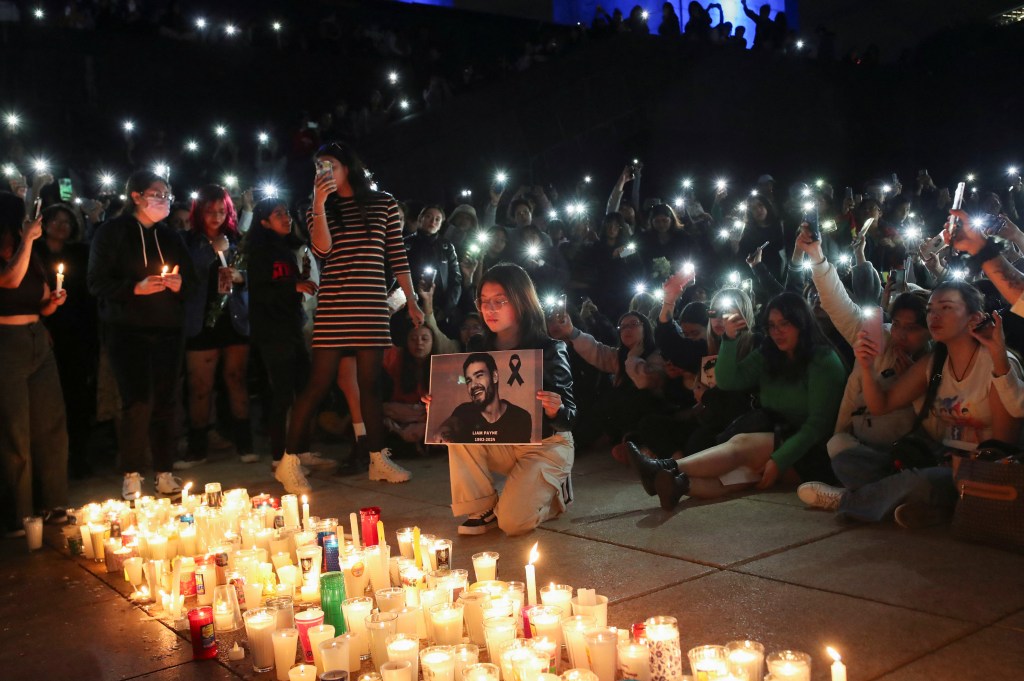 A woman holds a poster with an image of Liam Payne next to other One Direction fans as they gather to pay tribute to Liam Payne, at the Monument of the Revolution, in Mexico City, Mexico October 17, 2024. 