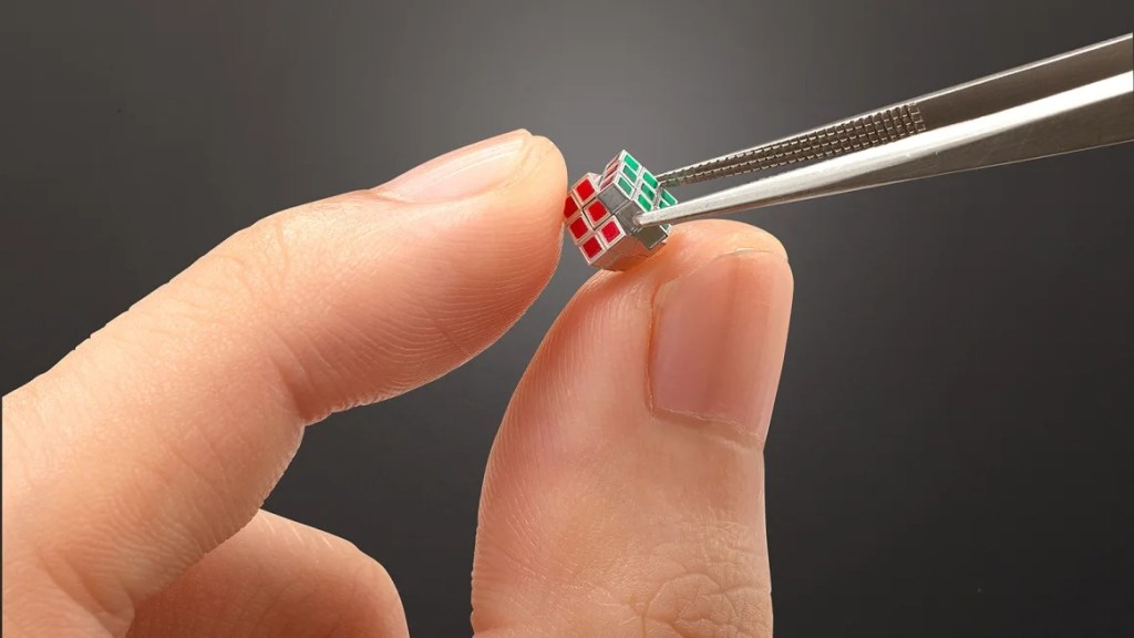 A person holding a tiny, functional Rubik's Cube with tweezers, made by Japanese toymaker MegaHouse.