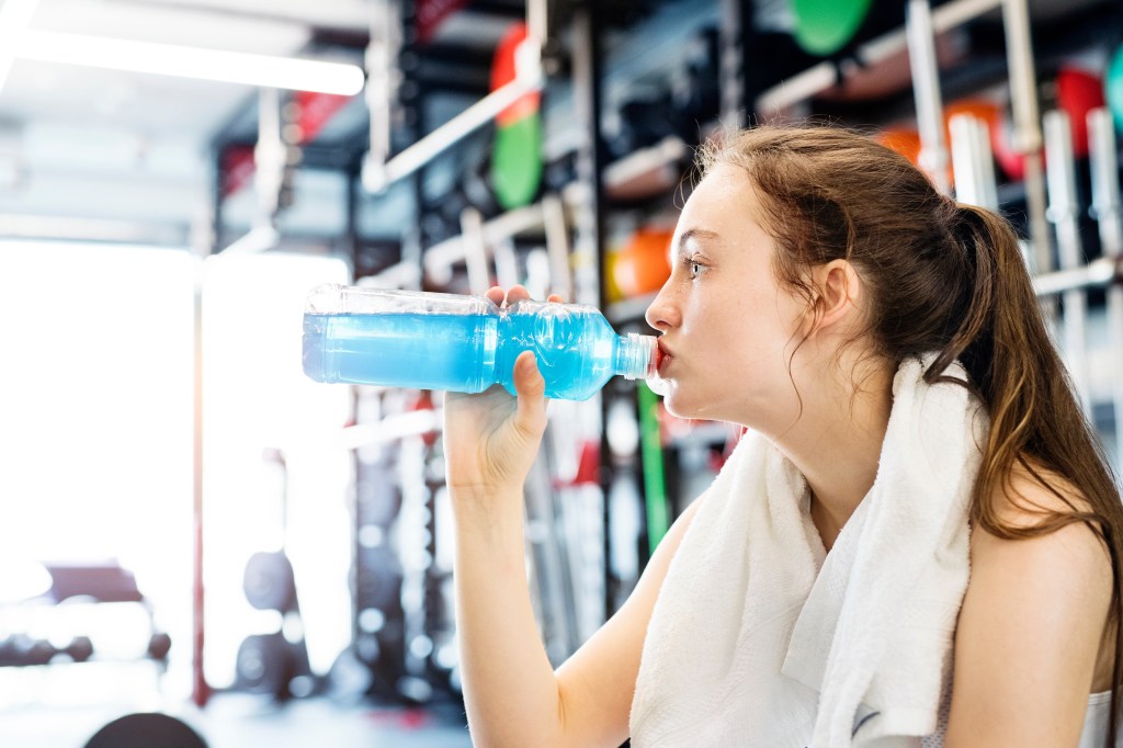 Young fitness girl with dental braces drinking water from a bottle in the gym after a hard workout