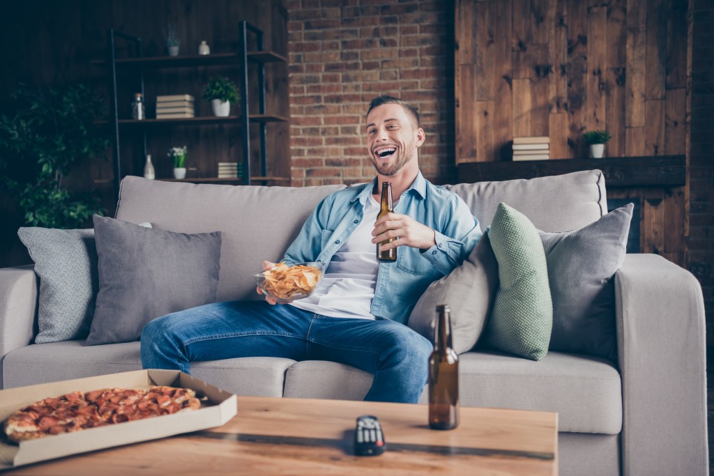Handsome guy staying home  to watch television, eat pizza and drink beer.
