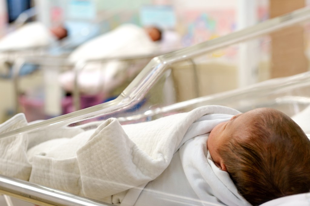 A newborn baby lies in a hospital bed.