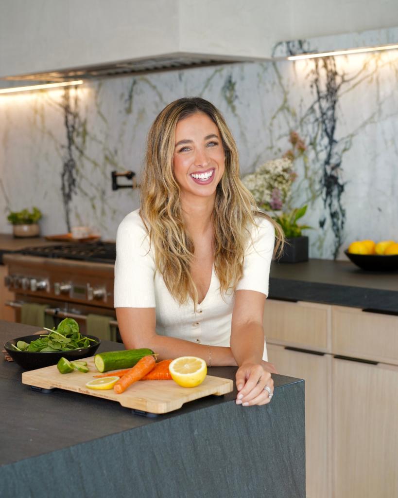 Katie Austin smiling for the camera with a chopping board of vegetables in a kitchen.