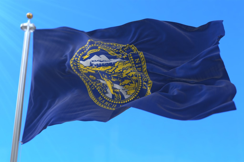 Nebraska man holding a blue flag with a yellow emblem in front of his house