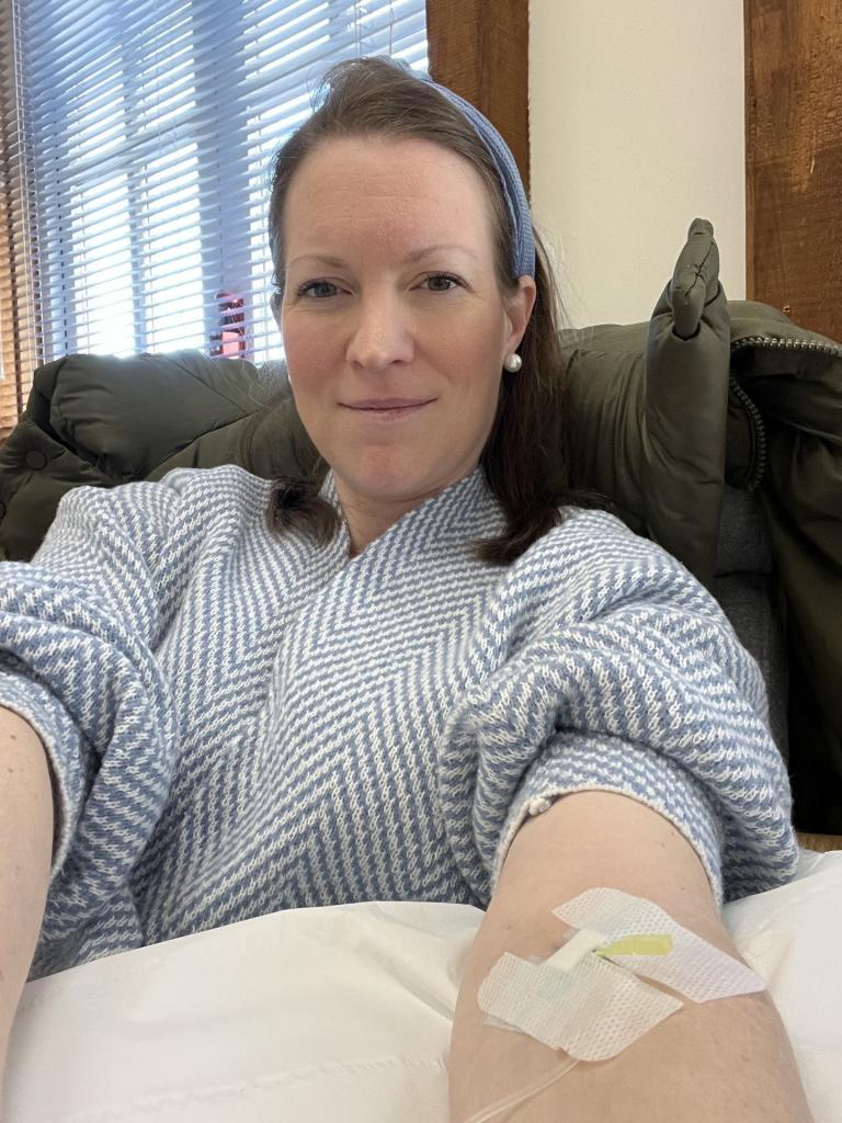 Zoe Gardner-Lawson smiles while undergoing treatment, an IV attached to her arm. 