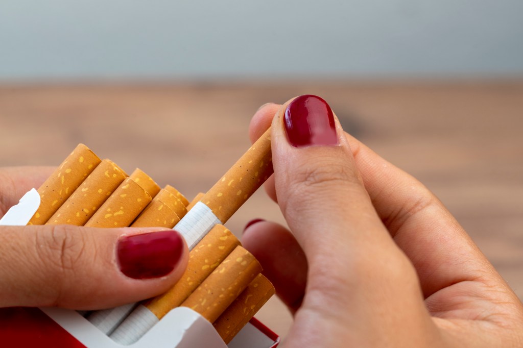 A person's hand holding a pack of cigarettes, symbolizing smoking issues and tobacco product reforms announced in 2022