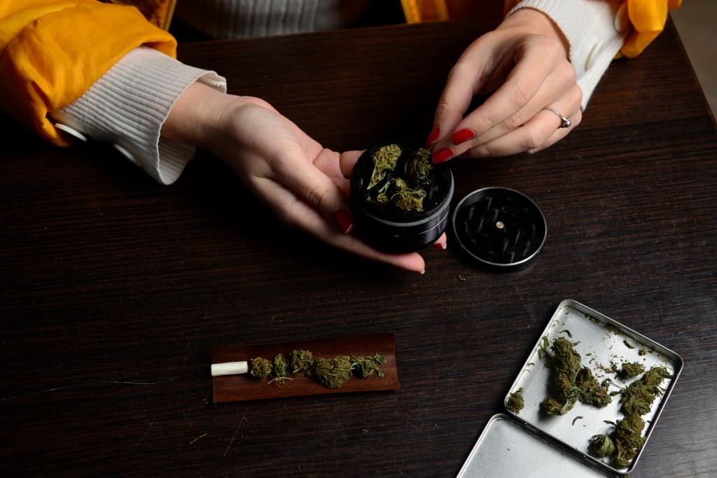 smoking weed with cigarette in hand and marijuana grinder on table