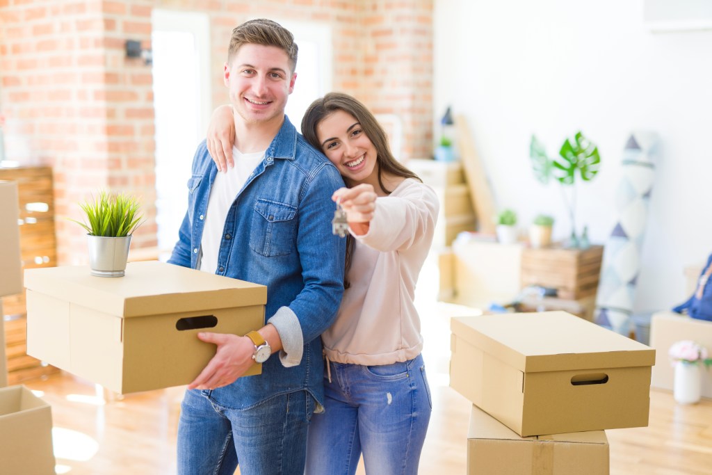 couple hugging in love and showing keys of new house, smiling happy moving to a new apartment