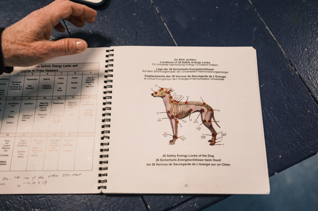 A volunteer, Susan Denis, holding a book illustrating animal pressure points, practicing Jin Shin Jyutsu therapy on rescue animals at the Southampton Animal Shelter.