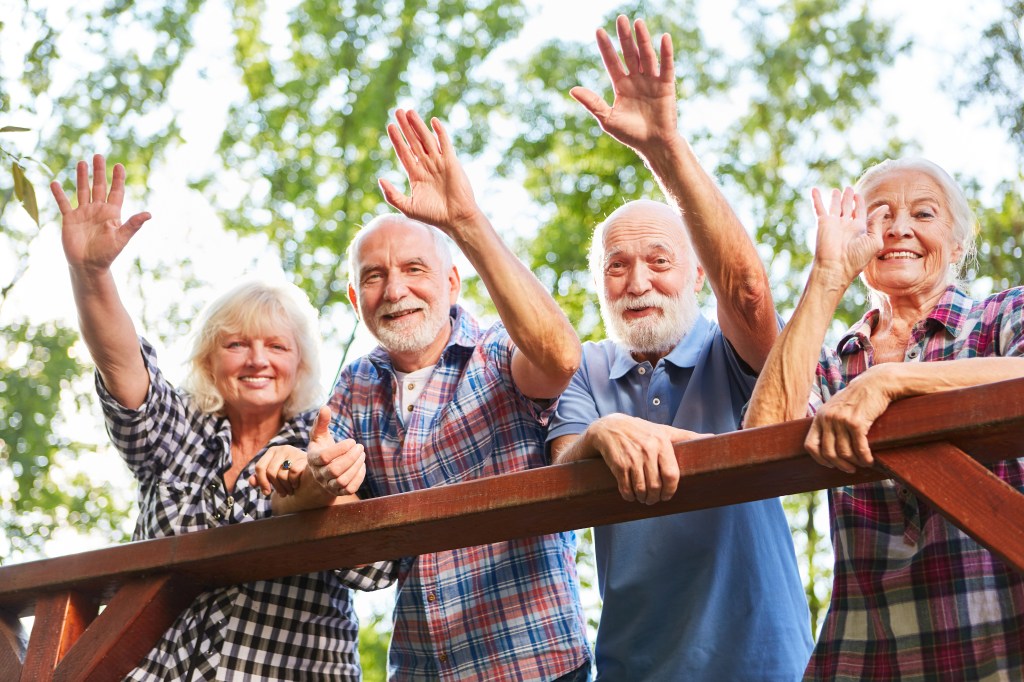 Cheerful seniors waving from a bridge on a summer outing. 