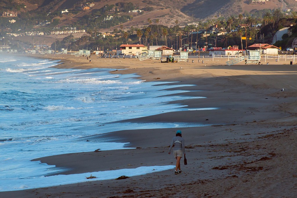 A person walking on Point Dume State Beach in California, with implied context of potential increase in squatting following wildfires