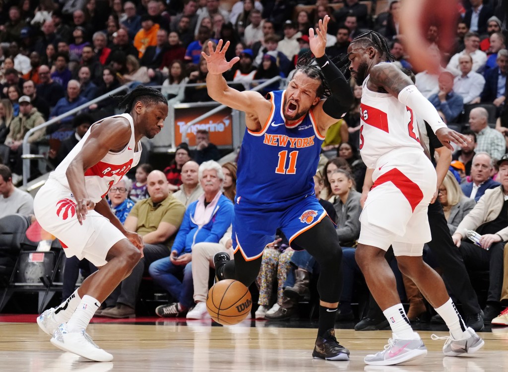 Knicks' Jalen Brunson is fouled while trying to dribble between Raptors' Jonathan Mogbo and Jamal Shead.