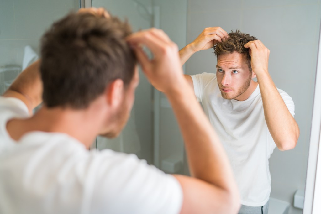 Man experiencing hair loss applying wax in front of bathroom mirror