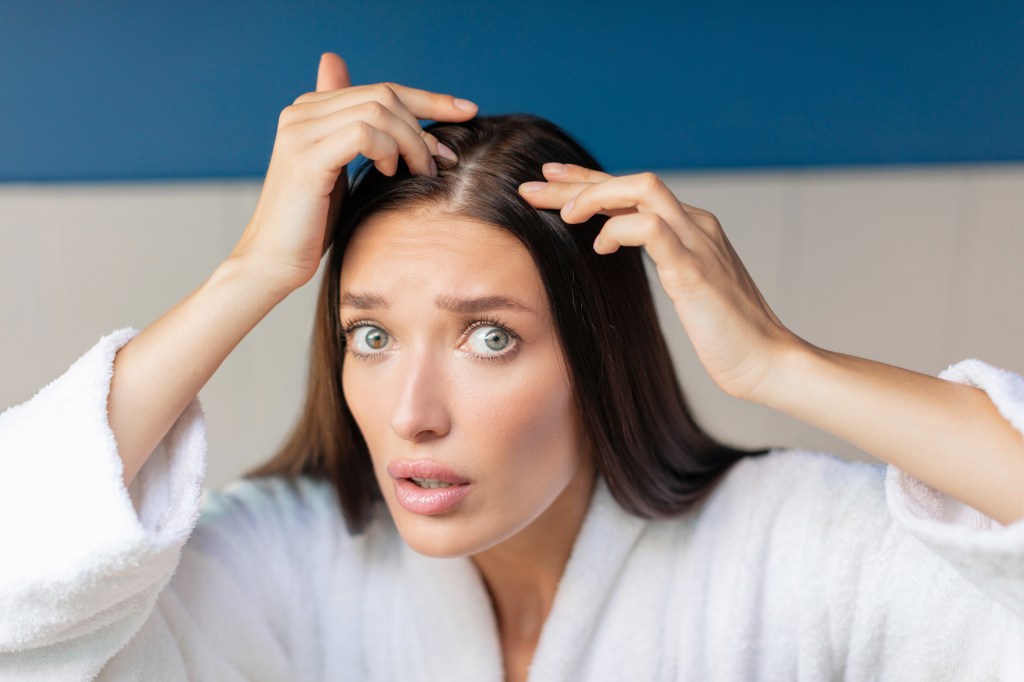 Young European woman looking at her scalp with worry about hair loss in a bathroom interior after shower