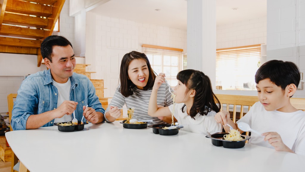 Asian family happily eating takeout together at home 