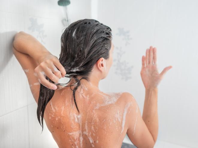 Woman experiencing hair loss while washing her hair in urban apartment