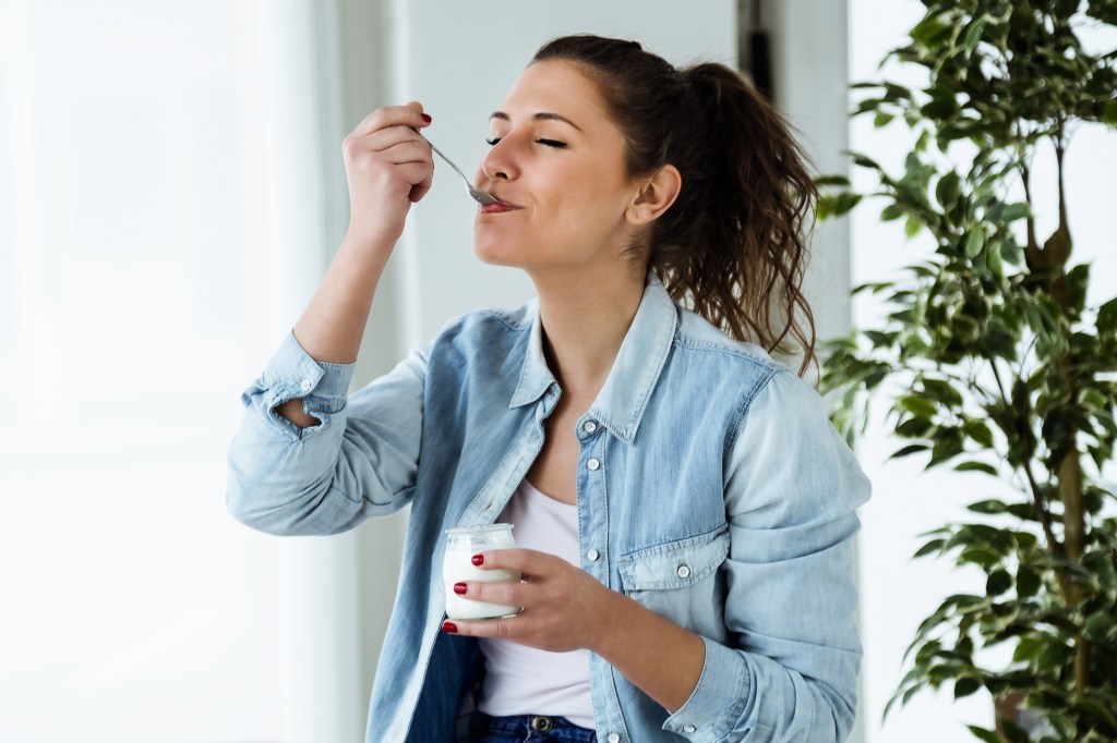 Young woman eating yogurt with a spoon at home