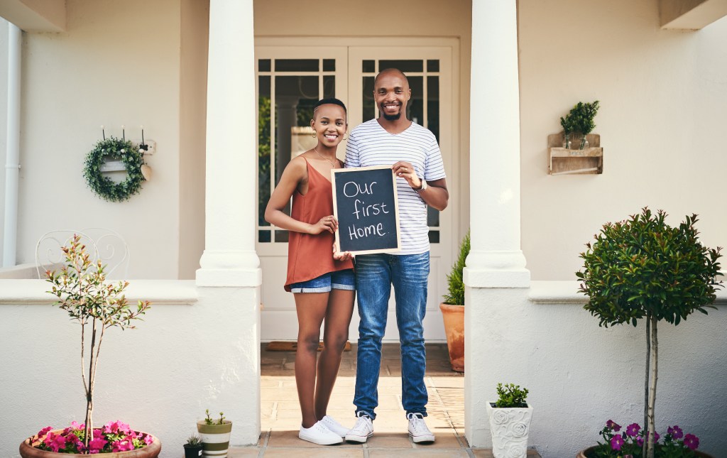 young couple holding a chalkboard with our first home written on it
