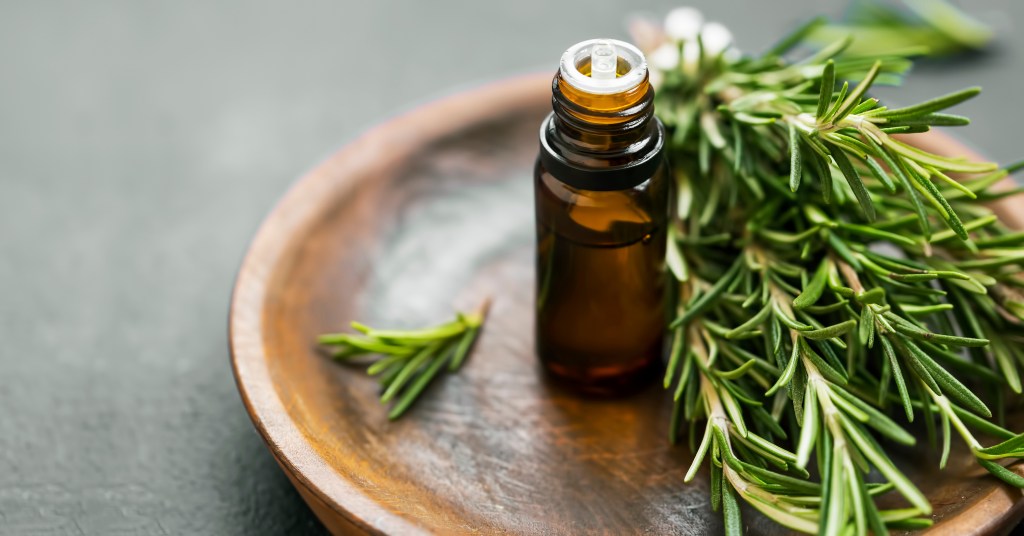 Rosemary essential oil bottle and rosemary herb bunch on a wooden plate, used for aromatherapy and hair loss prevention