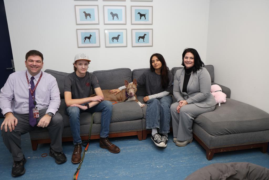 Stephen Ruisi, Robotics Club Advisor, Colin Heaney, Electronics Head, Tryla, a dog with three legs, Sarah Barros, President of the Southampton HS robotics team and Southampton HS Assistant Principle /Robotics Club Advisor Melissa Mitchel sitting on a couch.