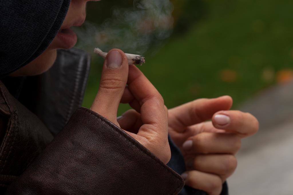 Young girl wearing a leather jacket smoking a joint