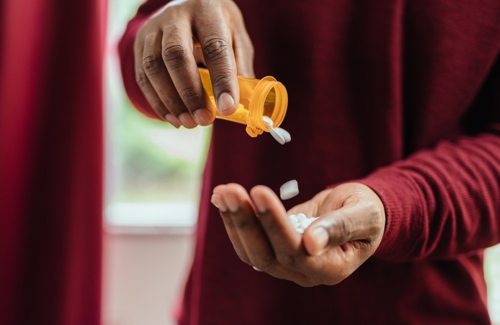 African American man in a red shirt pouring pills from a prescription bottle
