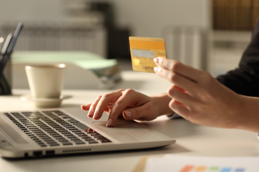 Executive hands holding a credit card and typing on a laptop at night