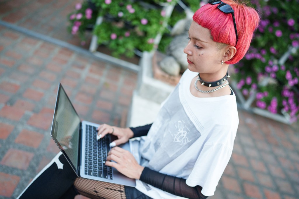 Gen z girl with pink hair leather fashion with punk Asian woman working remotely on laptop digital nomad in Thailand