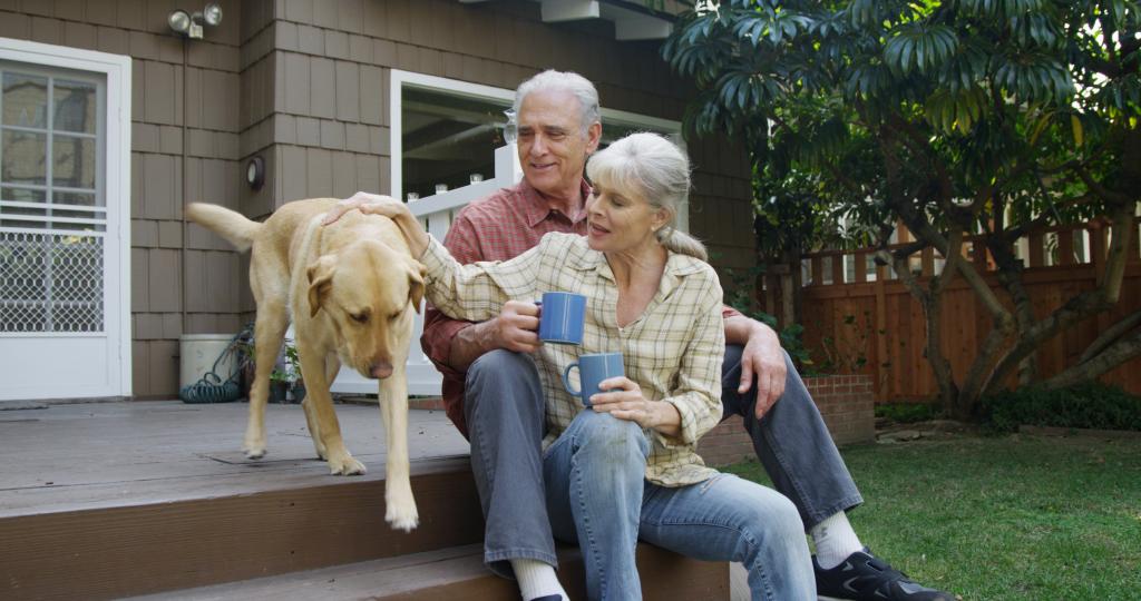 Senior couple having coffee petting dog in their yard