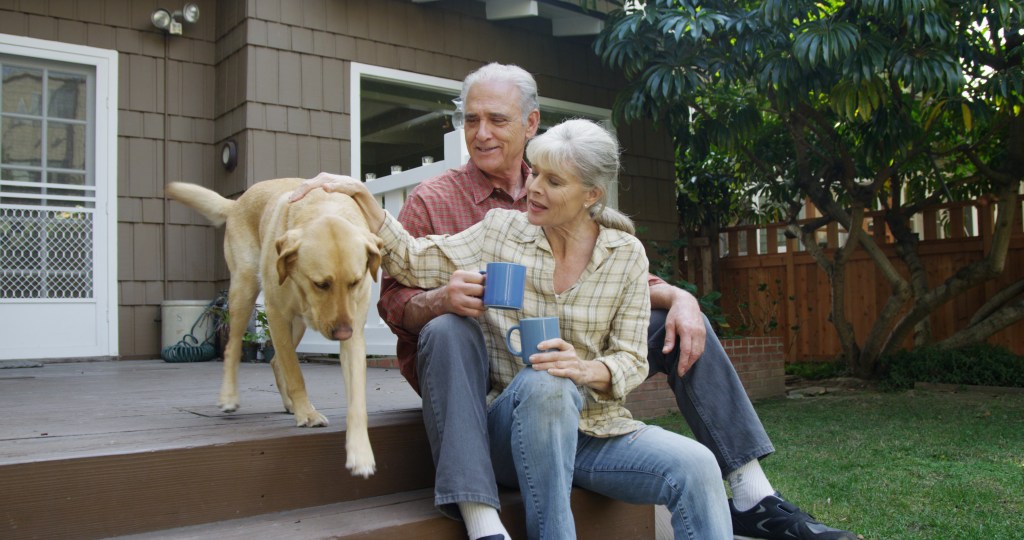 Senior couple having coffee petting dog in their yard
