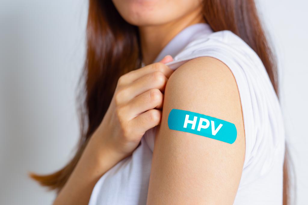 Teenage girl showing her arm with a blue bandage after receiving HPV vaccination