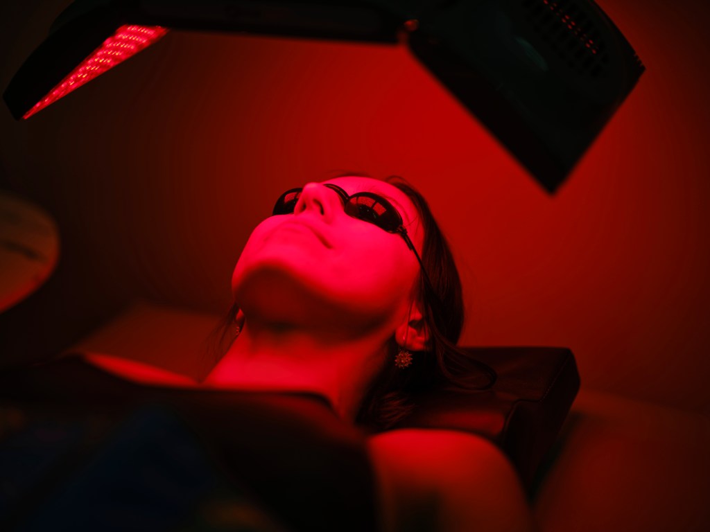 A woman on a bed, receiving LED red light therapy.