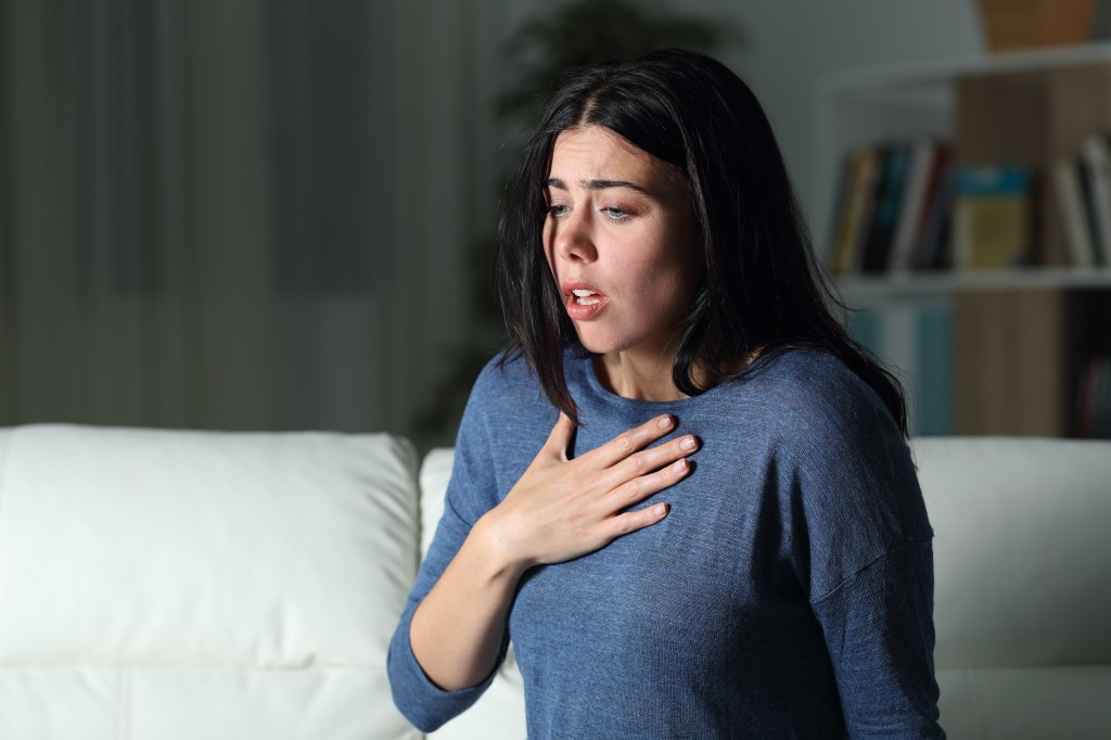A distressed woman alone at night, hand on her chest, experiencing an anxiety attack