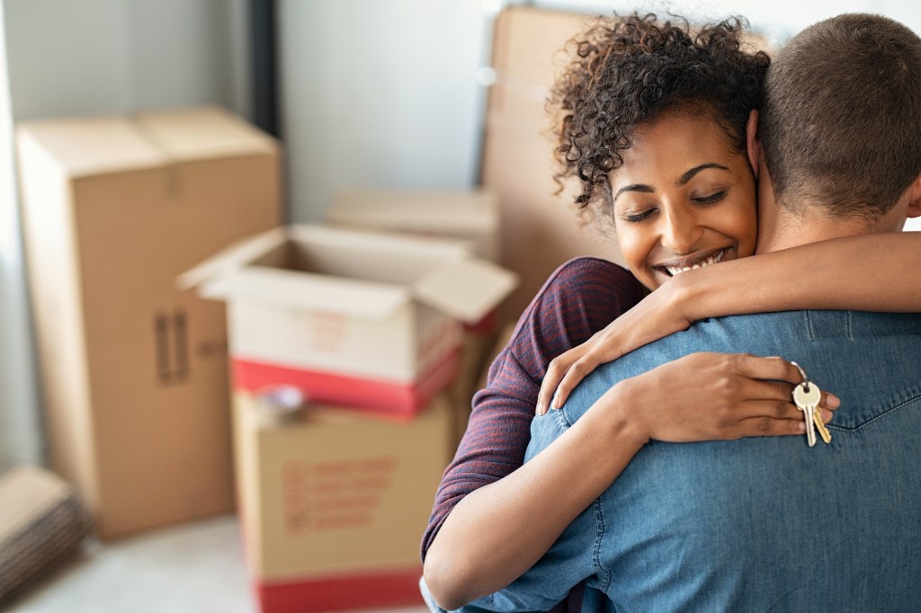 woman holding home keys while hugging boyfriend in their new apartment after buying real estate.
