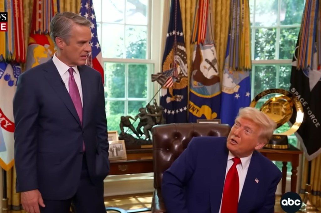 President Trump looks up at Terry Moran as the two are behind the Resolute Desk in the Oval Office.