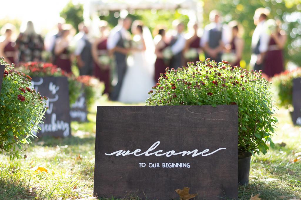 Rustic wooden welcome sign decorated with flowers for a wedding event outdoors