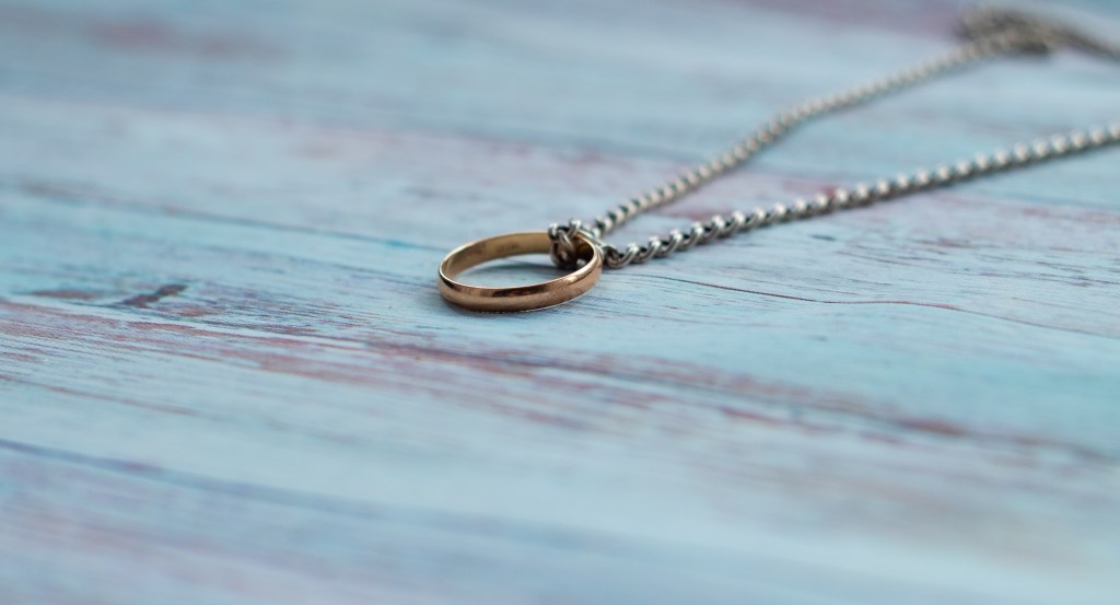 Silver chain and gold ring displayed on a wooden background