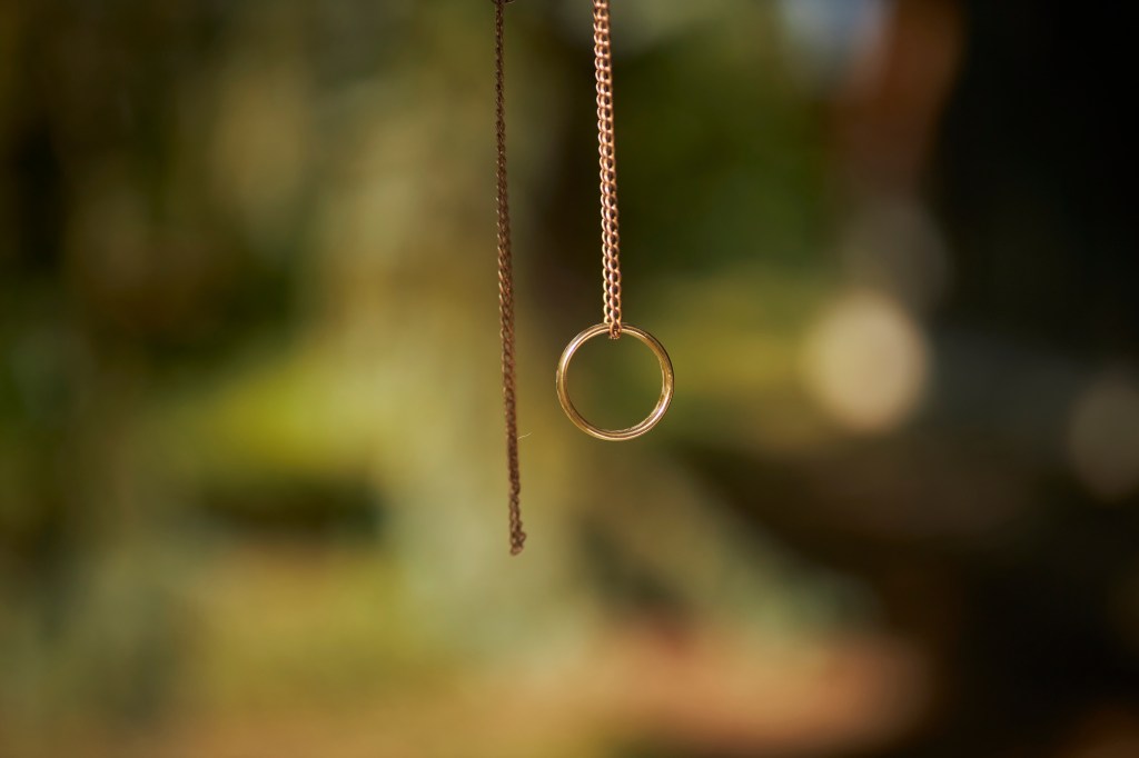 person holding a gold ring on a chain, lens focused in on it and blurred background