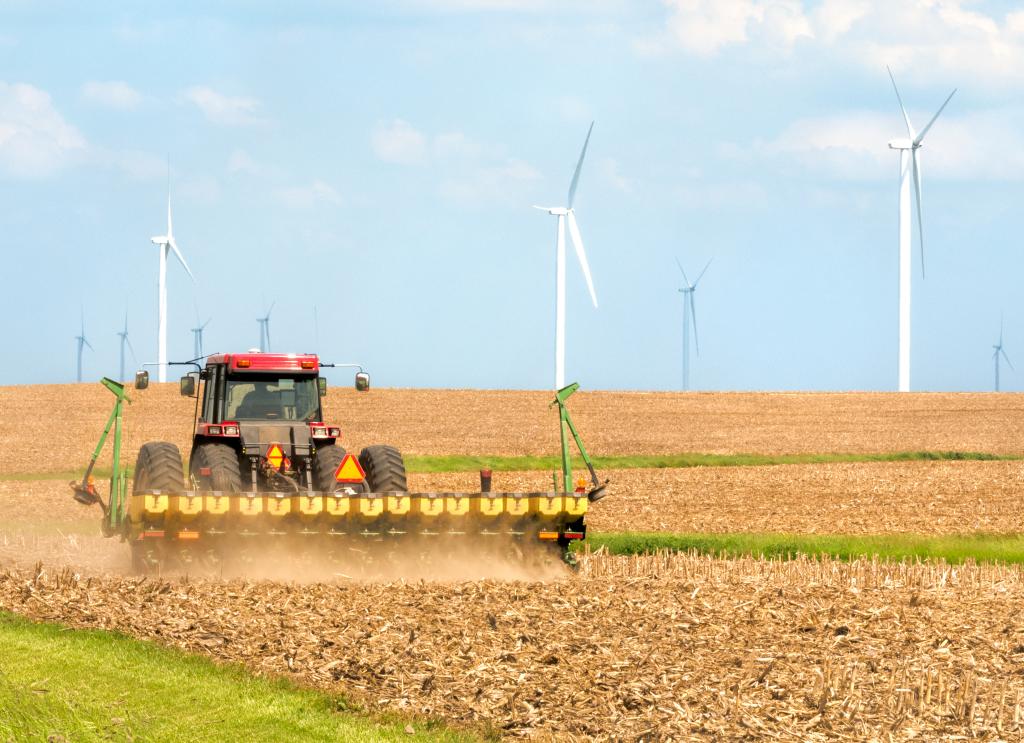 Farmer seeding soybeans from a tractor in a field near a wind farm in Danville, Illinois, Midwest USA.