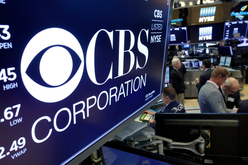 The CBS Corporation logo displayed above a trading post on the New York Stock Exchange floor, with a group of people including Tom Foreman nearby.